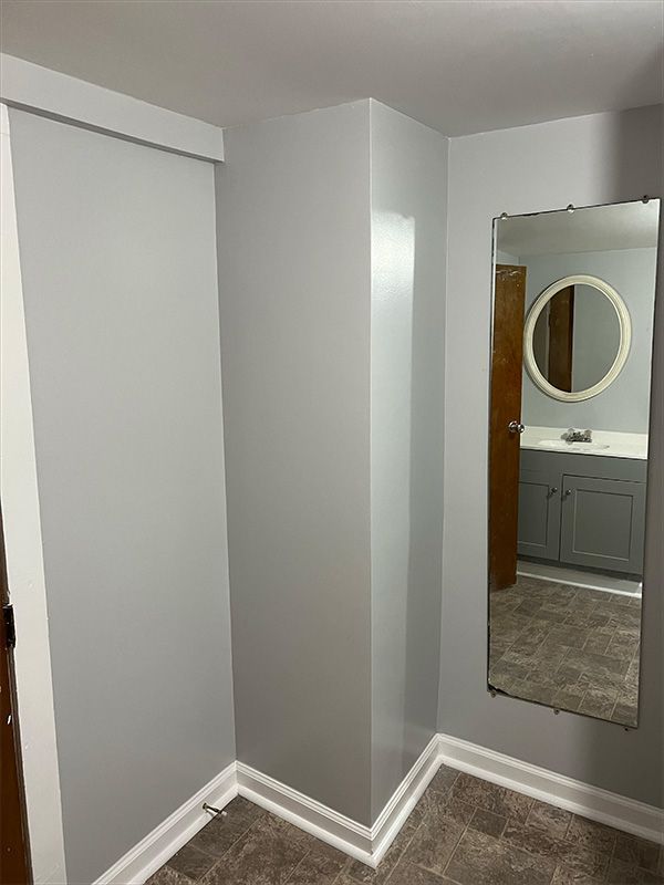 Corner of a room with gray walls, a mirror, and a glimpse into a gray-themed bathroom.