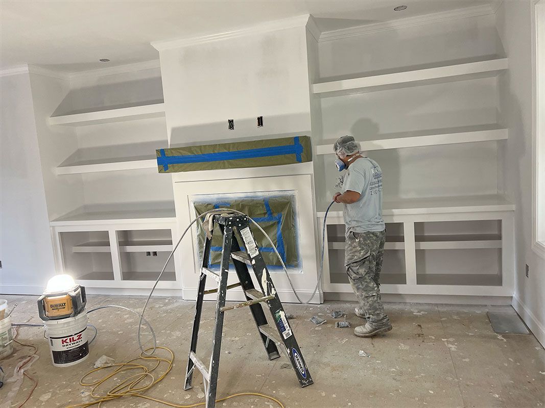 A person painting a white bookshelf unit with a fireplace. The room is under construction.