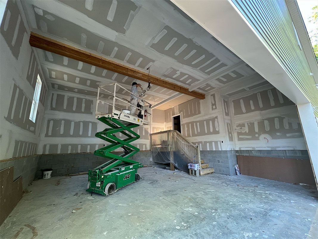 Green scissor lift inside a garage during drywall installation.