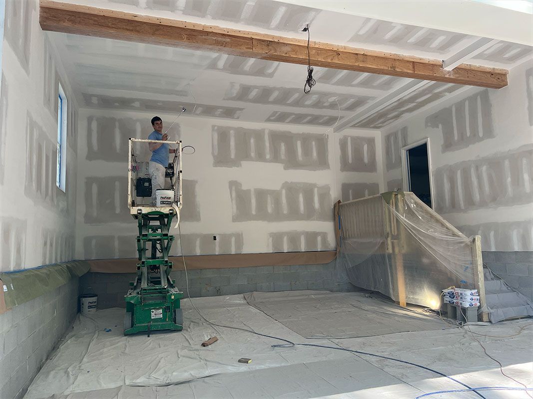 Person on lift working on drywall in garage. Unfinished walls and ceiling.