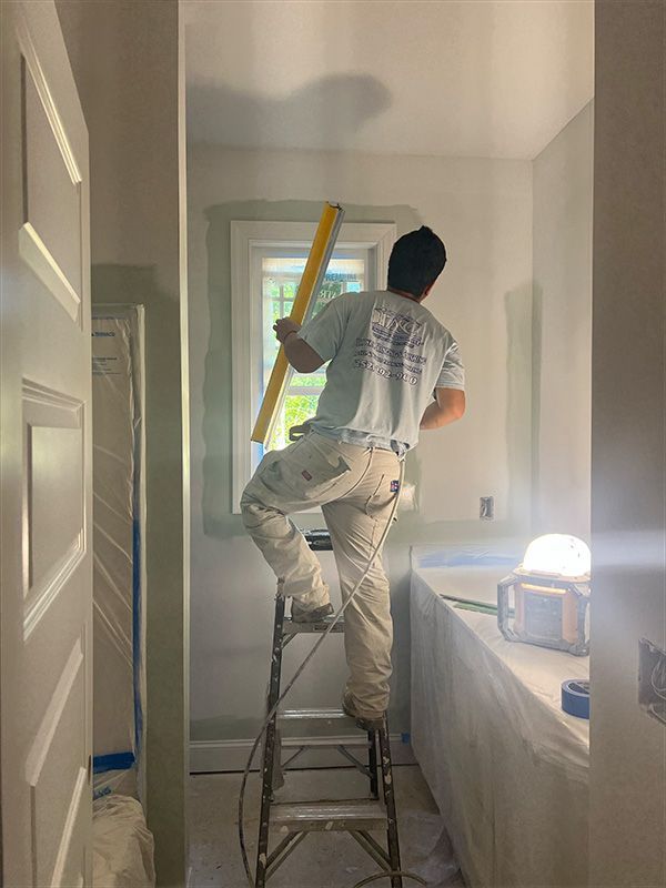 Person on a ladder uses a level on a window frame in a room being painted.