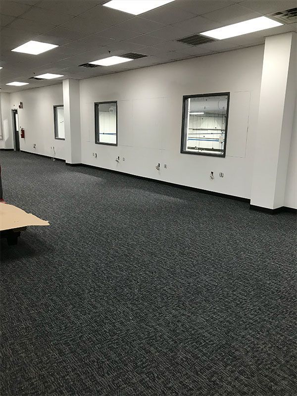 Empty office space with dark carpet, white walls, three windows, and overhead lights.
