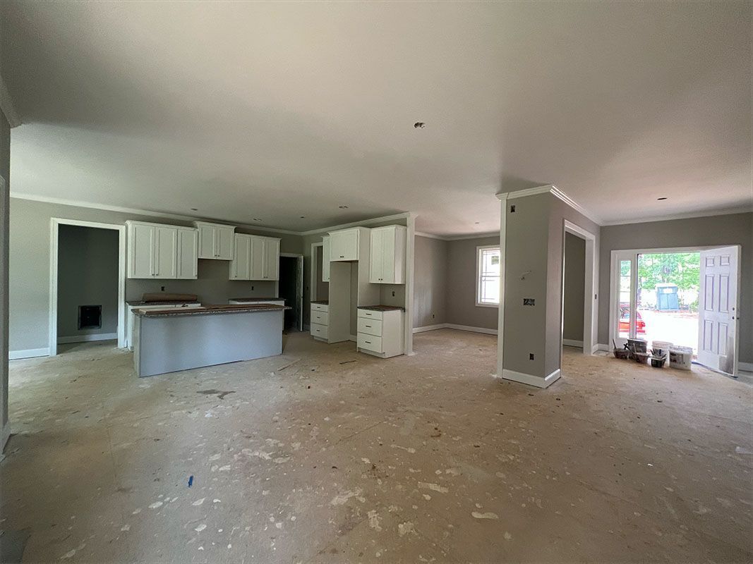 Interior of a home, showing unfinished kitchen with white cabinets, gray island, and doorway to the outside.