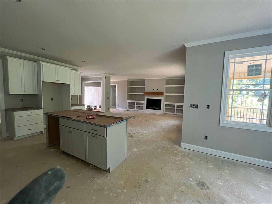 Interior of a new home under construction; kitchen with island, living area with fireplace and built-in shelving.