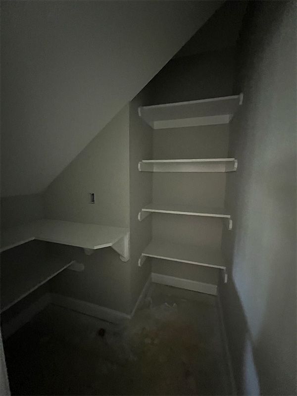 A small closet with built-in white shelves and a sloped ceiling. The walls are light grey.