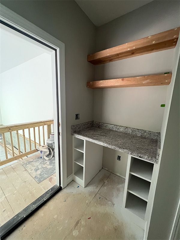 Built-in desk with granite countertop and shelving, unfinished room with balcony access.