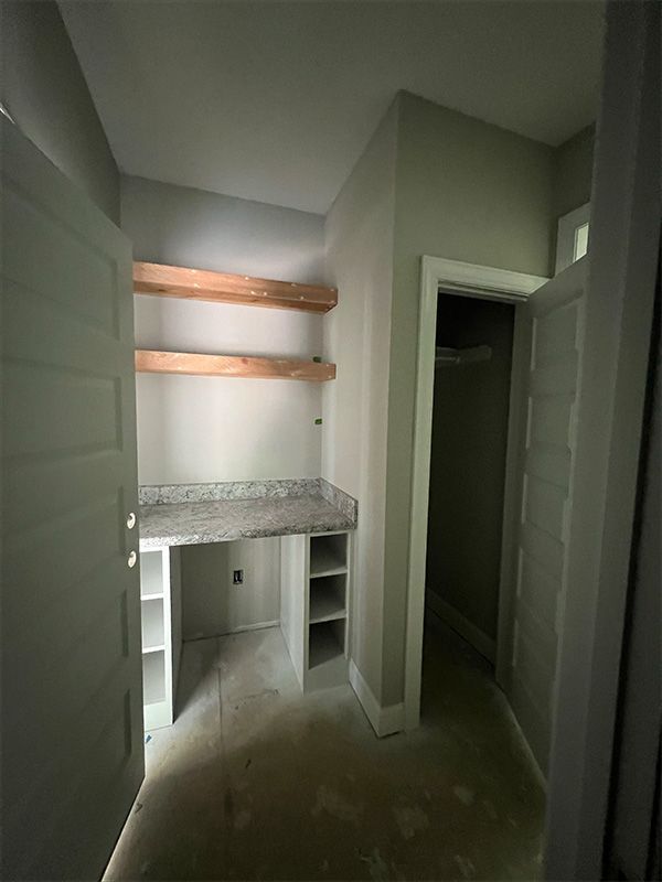 An empty walk-in closet with built-in desk and open shelving. Light gray walls and white trim.