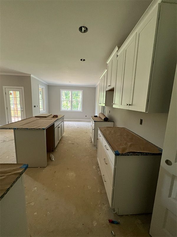 Unfinished kitchen with light gray cabinets, countertops covered, and two islands.