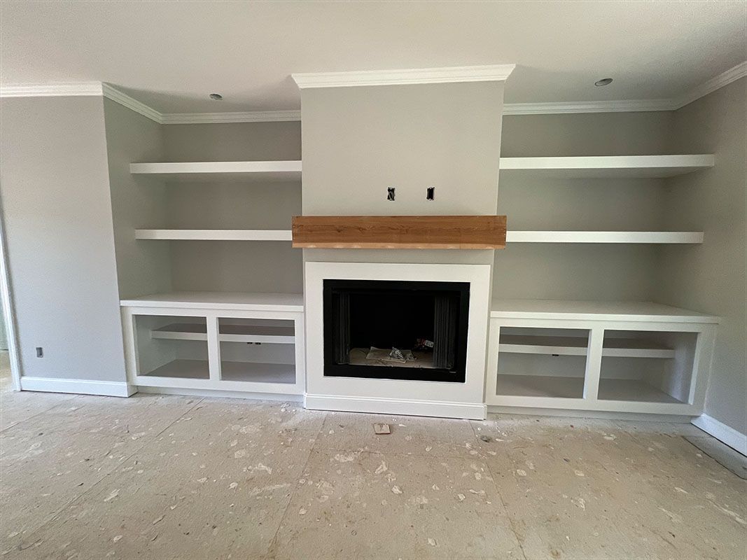 Fireplace with built-in bookshelves painted white, centered in a room with light grey walls and flooring.