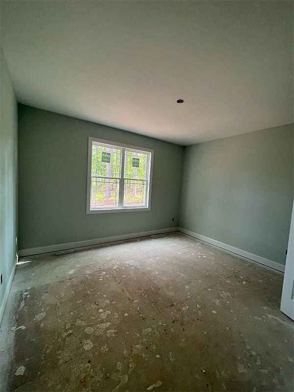 Empty room with light green walls, a window, and a dirty concrete floor.