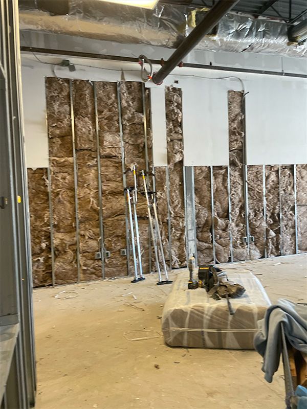 Interior construction site with exposed insulation in wall, metal studs, and drywall. 