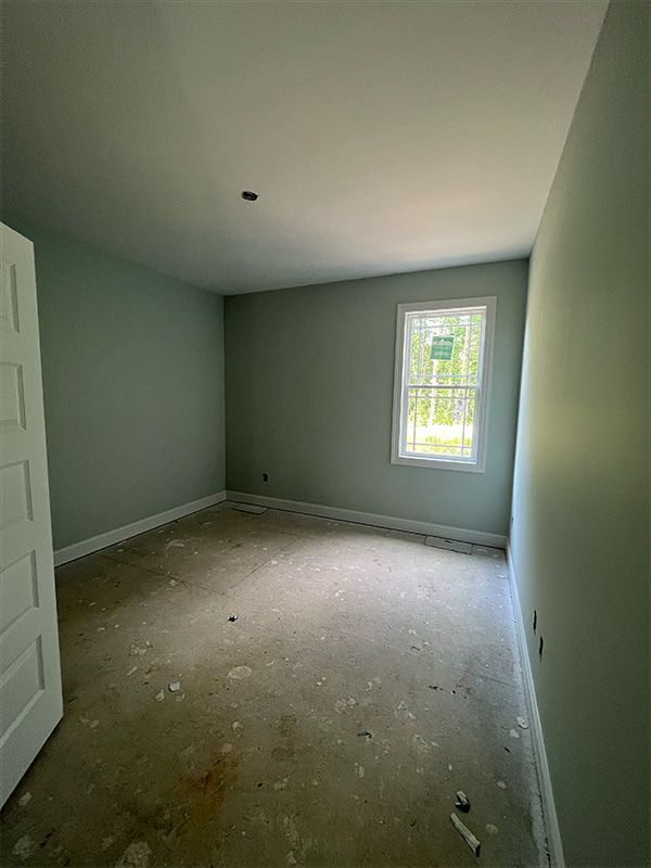 Empty room with pale green walls, white trim and window, concrete floor, white door.