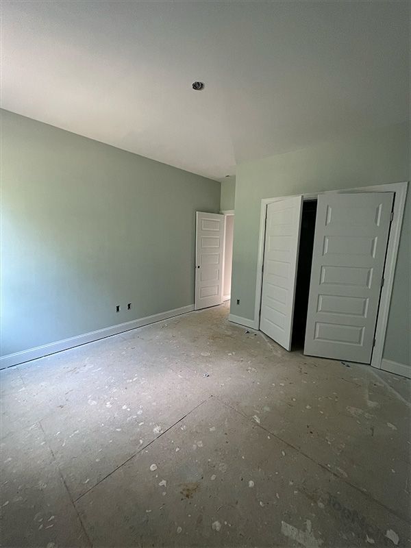 Empty room with sage green walls, white doors, and unfinished floor.