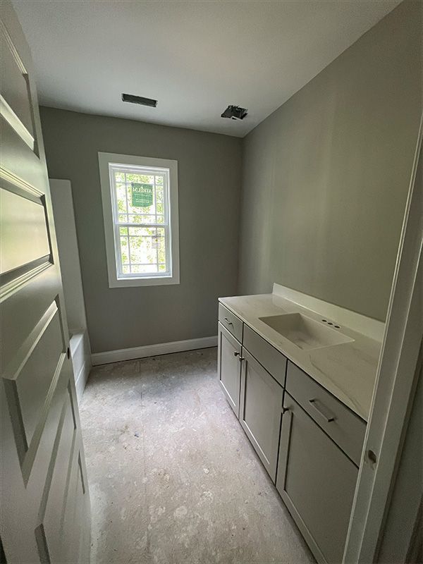 Empty bathroom with a white vanity and window, light gray walls, and unfinished floor.