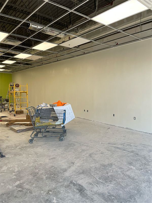 Interior of a building under construction, showing a concrete floor, painted wall, and exposed ceiling.