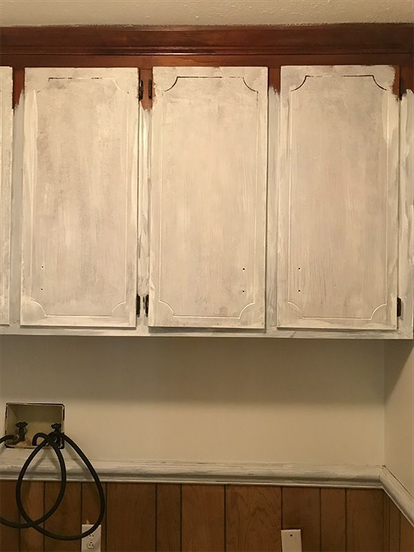 White-painted kitchen cabinets above a lower wall with wood paneling and a dark cable.