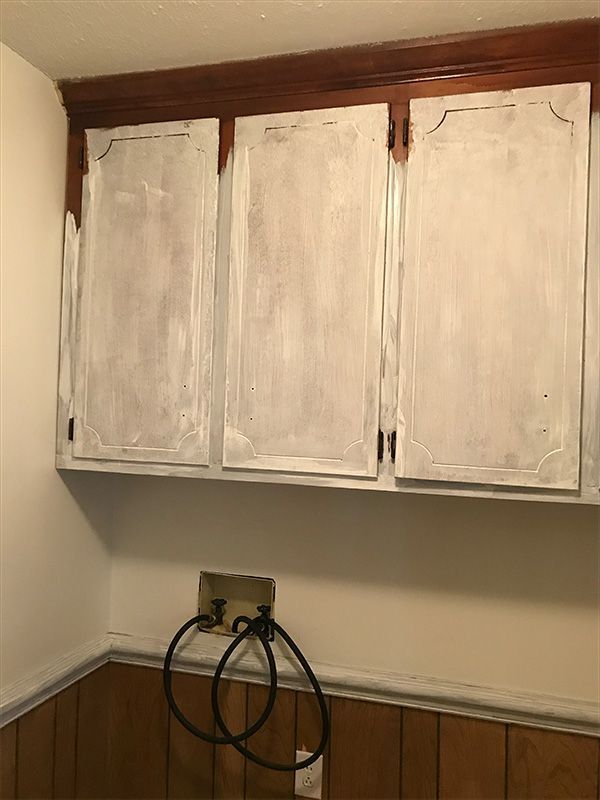 White-painted kitchen cabinets above a wall with wood paneling.