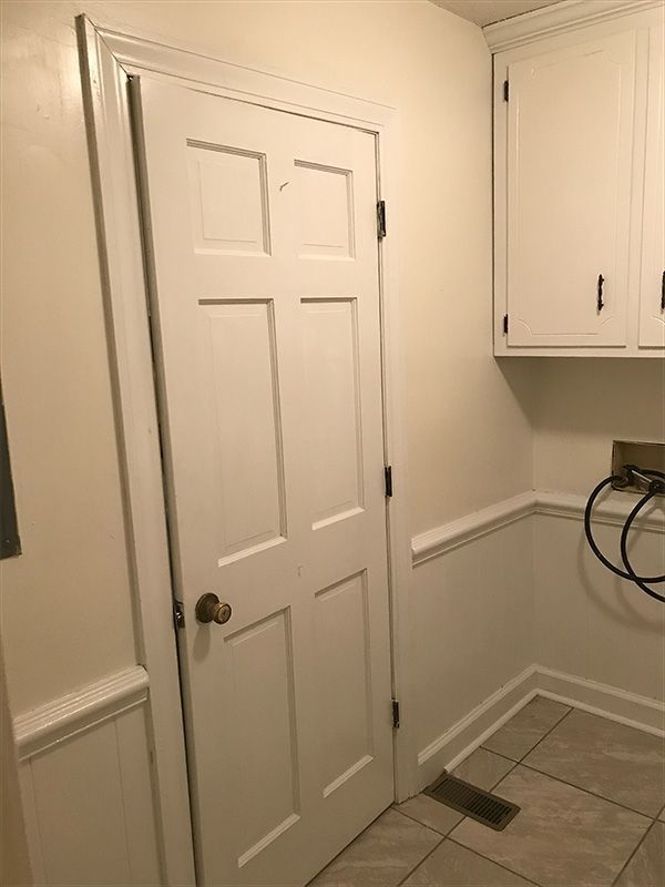 White door slightly ajar in a room with white walls, cabinets, and a tiled floor.