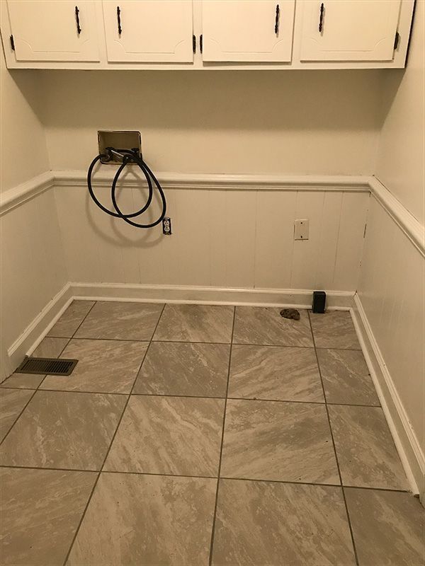Empty laundry room with off-white walls, tiled floor, and overhead cabinets. 