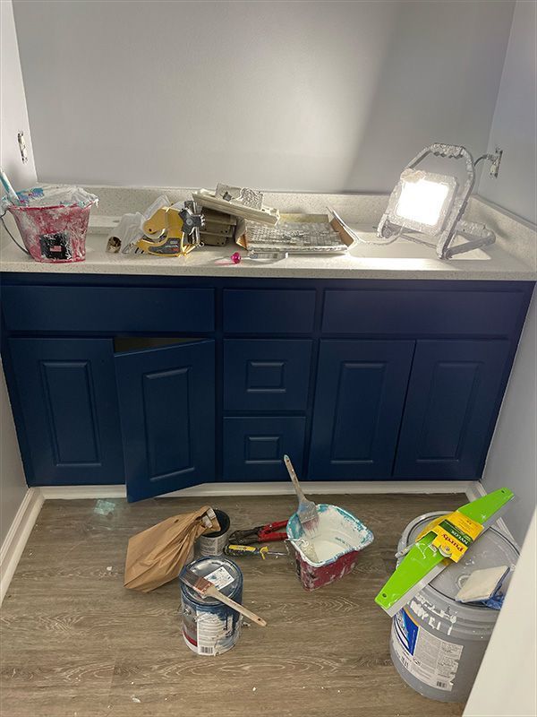 Bathroom vanity undergoing renovation; blue cabinets, gray walls, tools, and paint on floor.