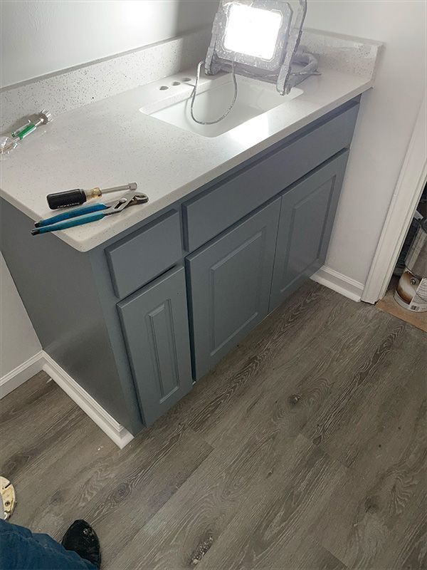 Gray bathroom vanity with white countertop, tools, and a work light.
