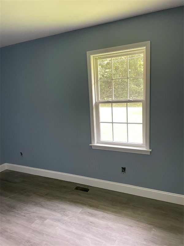Blue-painted room with white trim, window, and gray flooring.