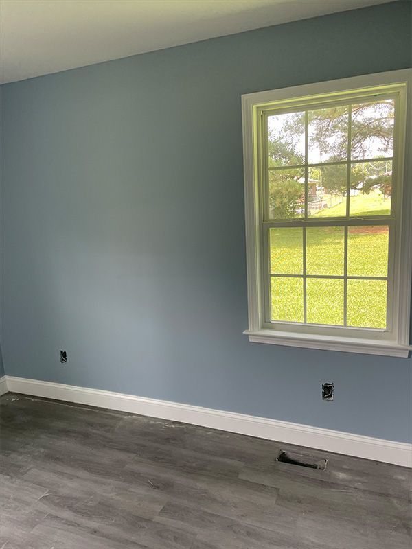 Blue painted room with white trim, window, and gray flooring.