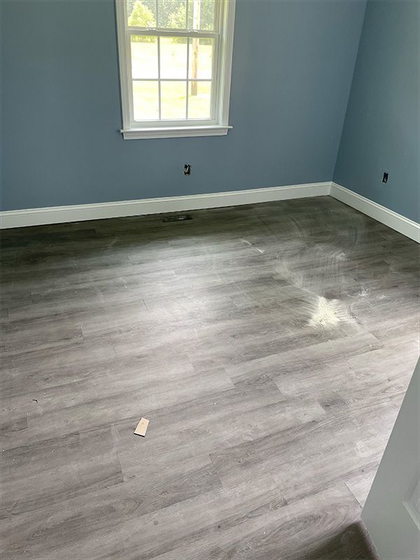 Empty room with gray wood-look flooring, blue walls, white trim, and a window.