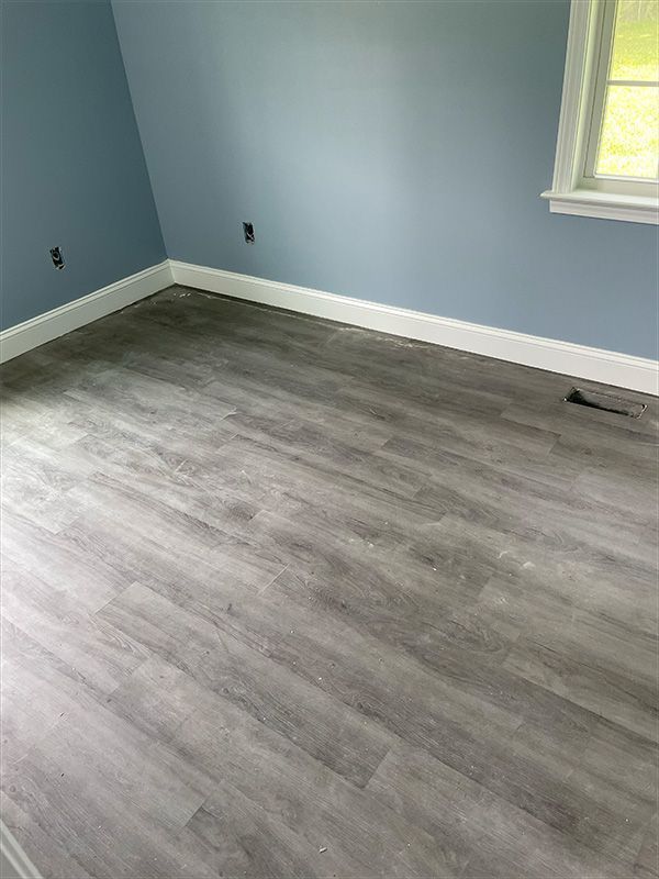 Room with light grey wood-look flooring, light blue walls, white trim, and a window.
