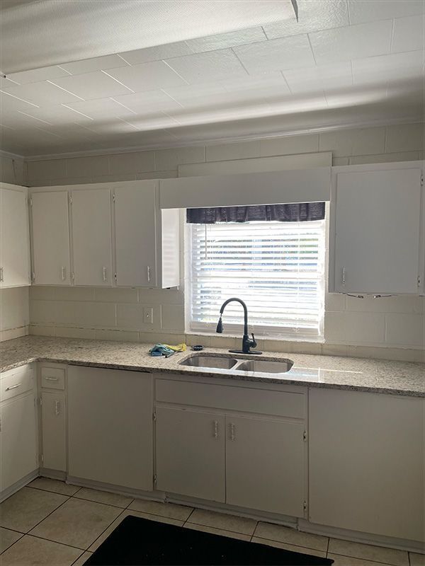White kitchen with cabinets, sink, window with blinds, and countertop.