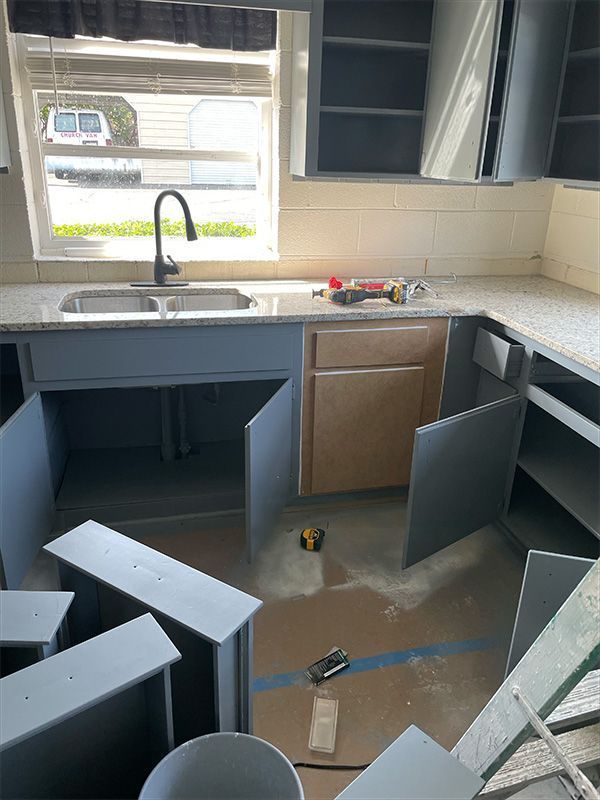 Kitchen cabinets in various states of assembly, light blue-gray paint. 