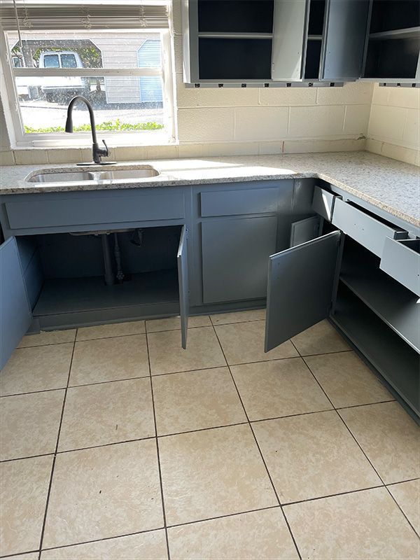 Partially constructed kitchen with gray cabinets, a sink, and open doors. 