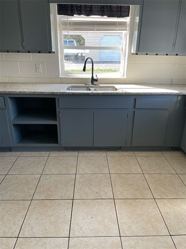 Kitchen with blue cabinets, white countertops, a window, and tile floors.