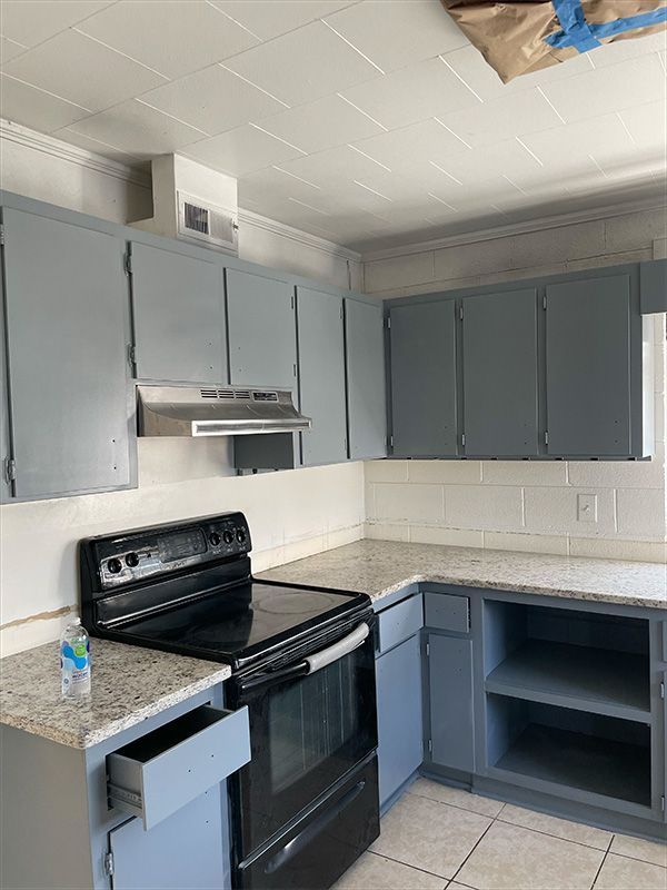 Kitchen with gray cabinets, black stove, granite countertops, and white backsplash.