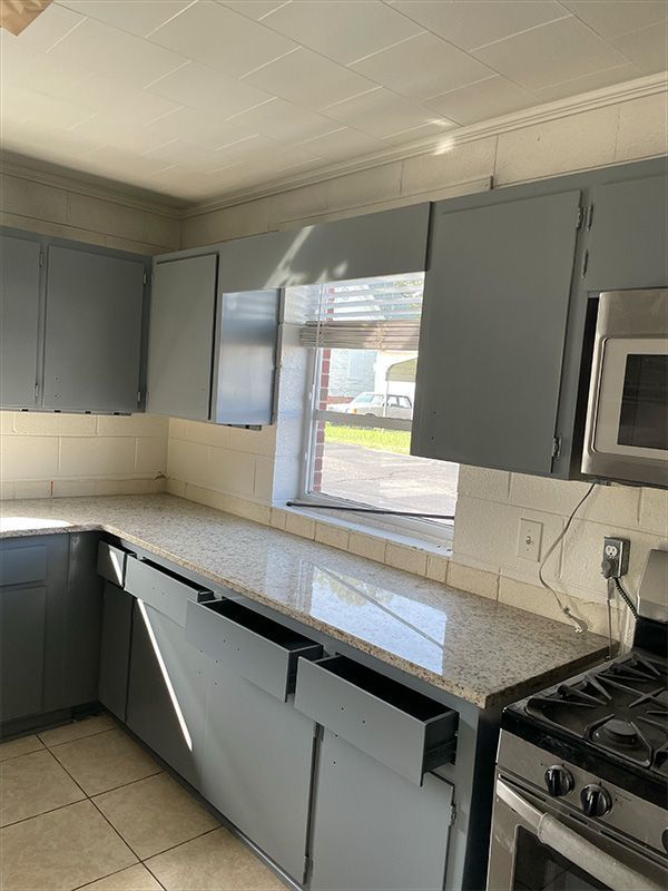 Kitchen with gray cabinets, granite countertops, window, and stainless steel oven.