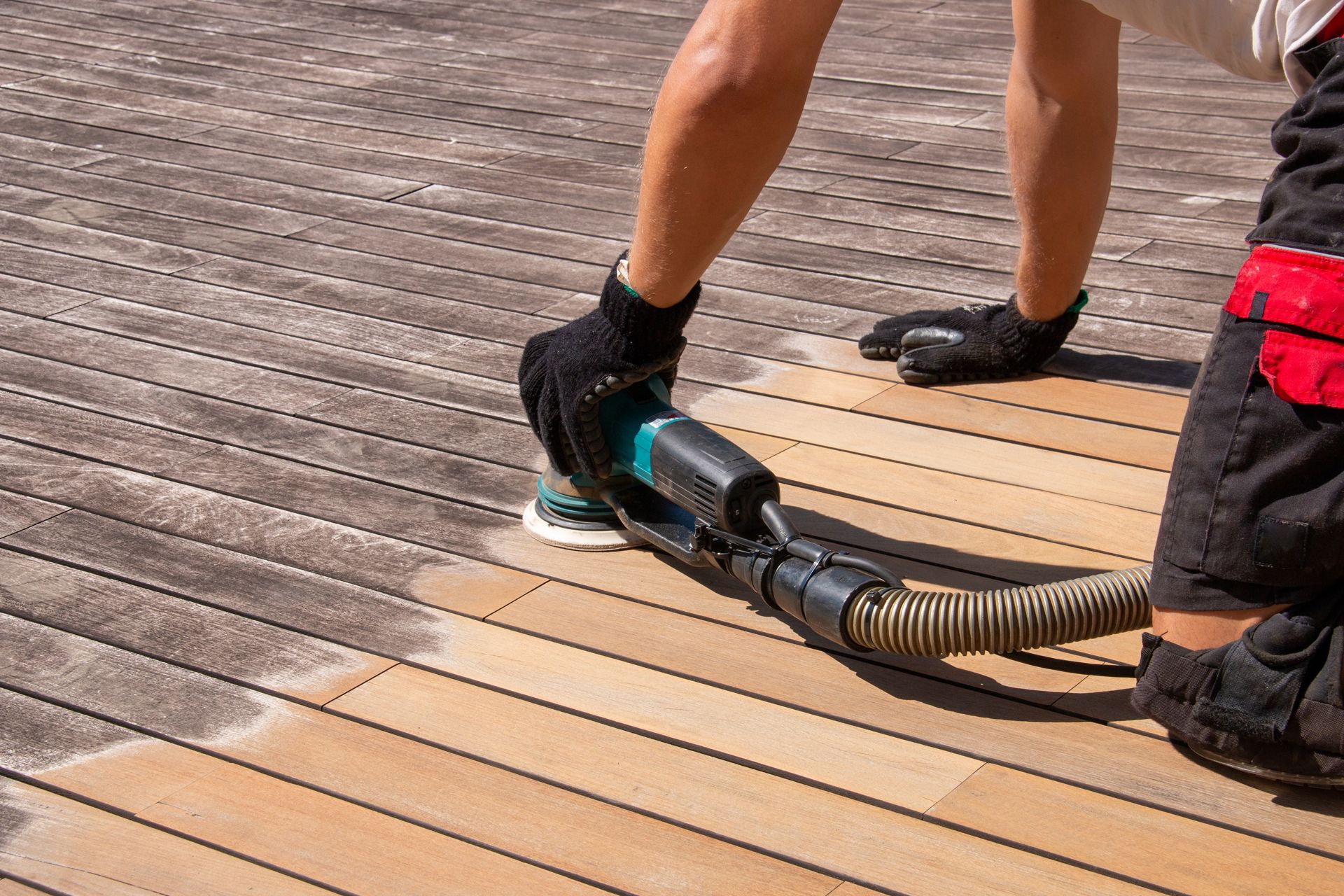 Person sanding a wooden deck with a power sander.