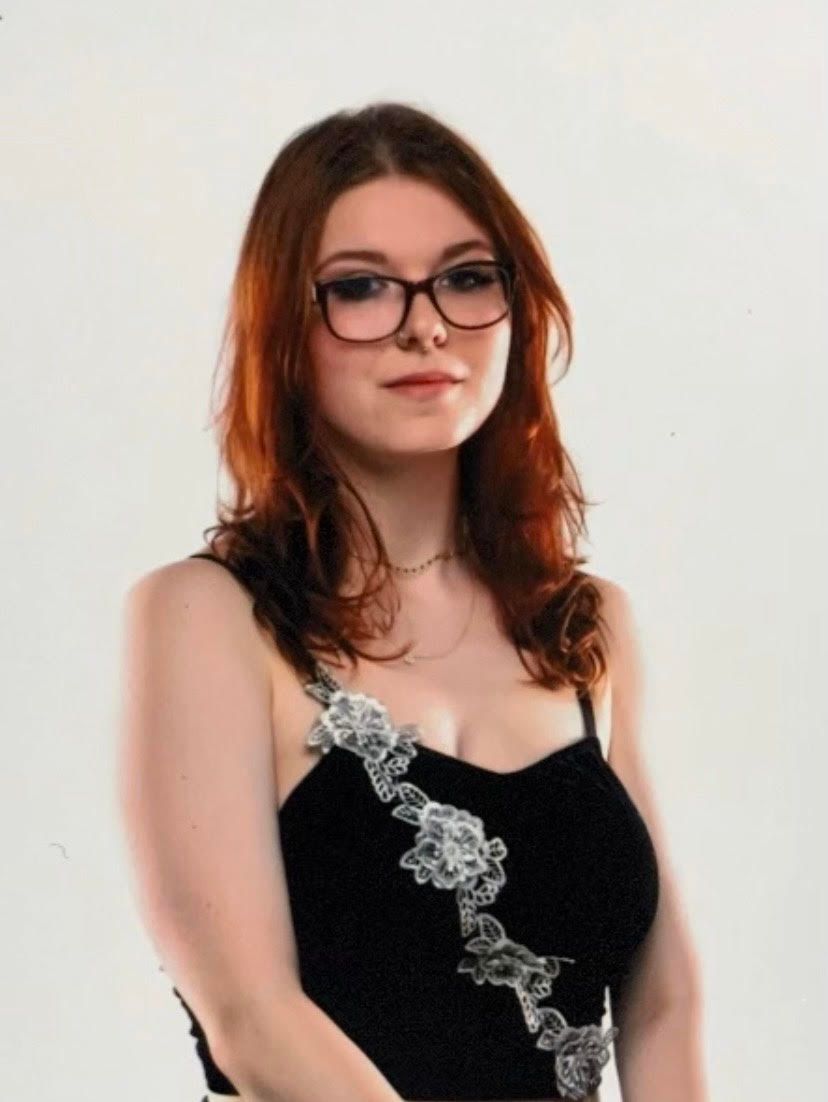 A woman with red hair wearing glasses and a black top