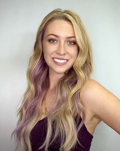 a woman with blonde and purple hair is smiling for the camera .
