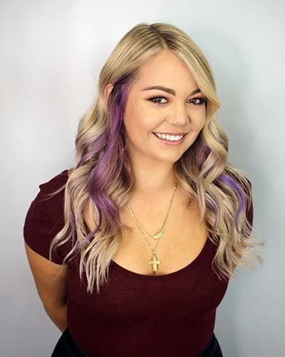 a woman with blonde and purple hair is wearing a necklace and smiling .