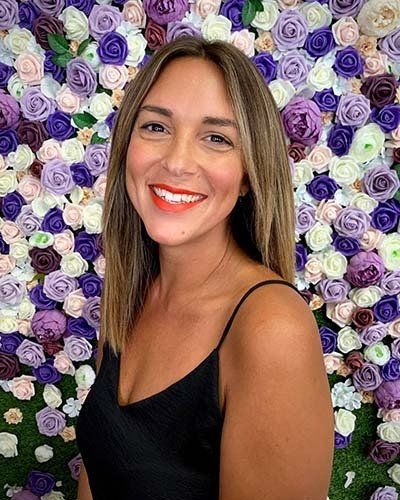 a woman is smiling in front of a wall of purple and white flowers .
