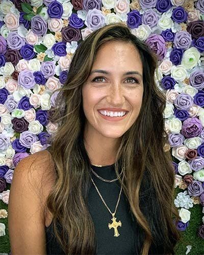 a woman is smiling in front of a wall of flowers .