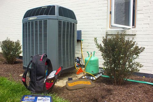 A backpack is sitting on the grass next to an air conditioner.
