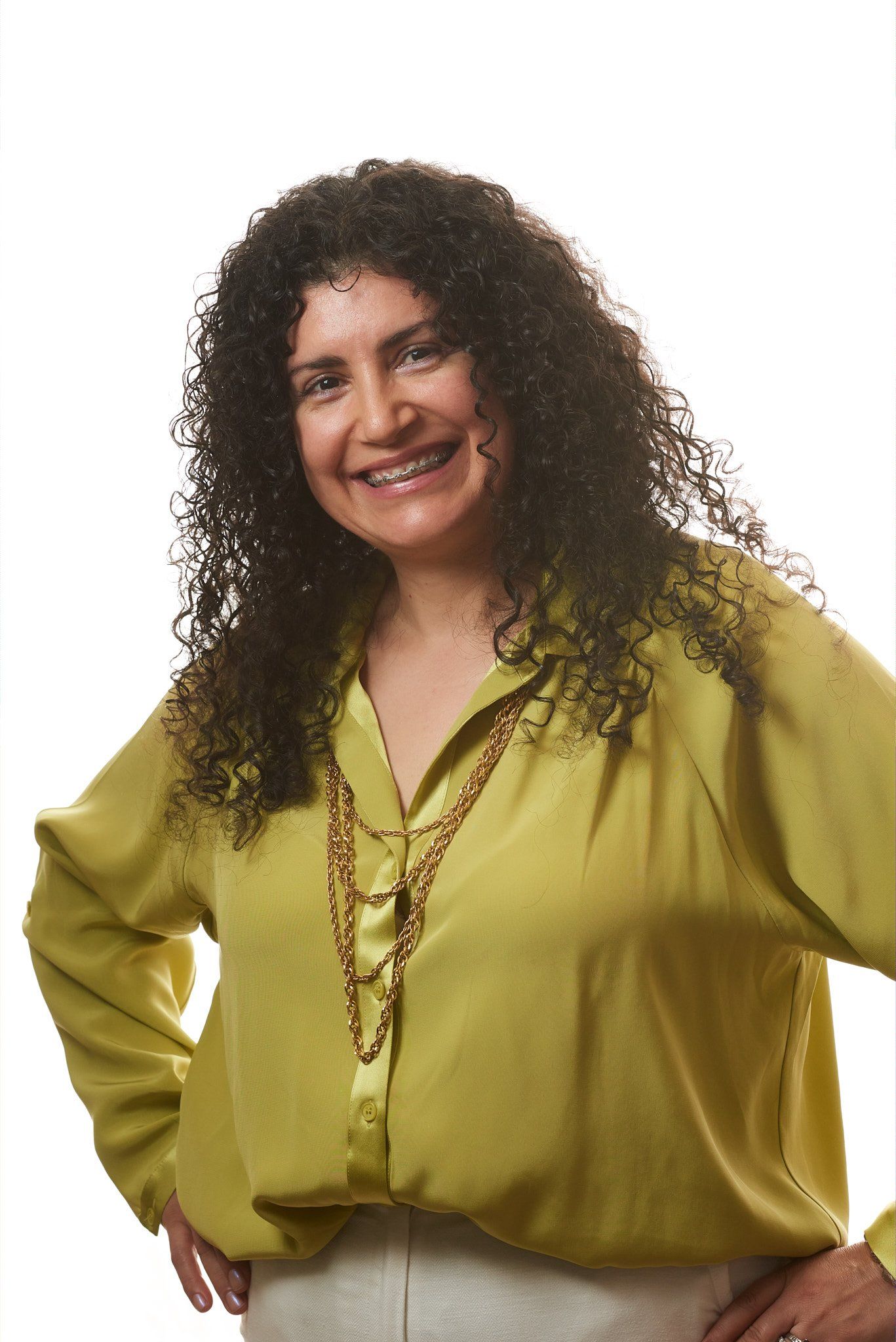 A woman with curly hair is wearing a green shirt and a gold necklace.