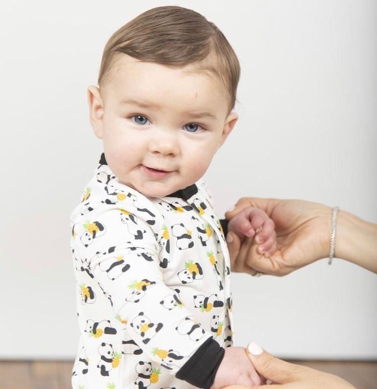 A woman is holding a baby 's hand while looking at the camera.