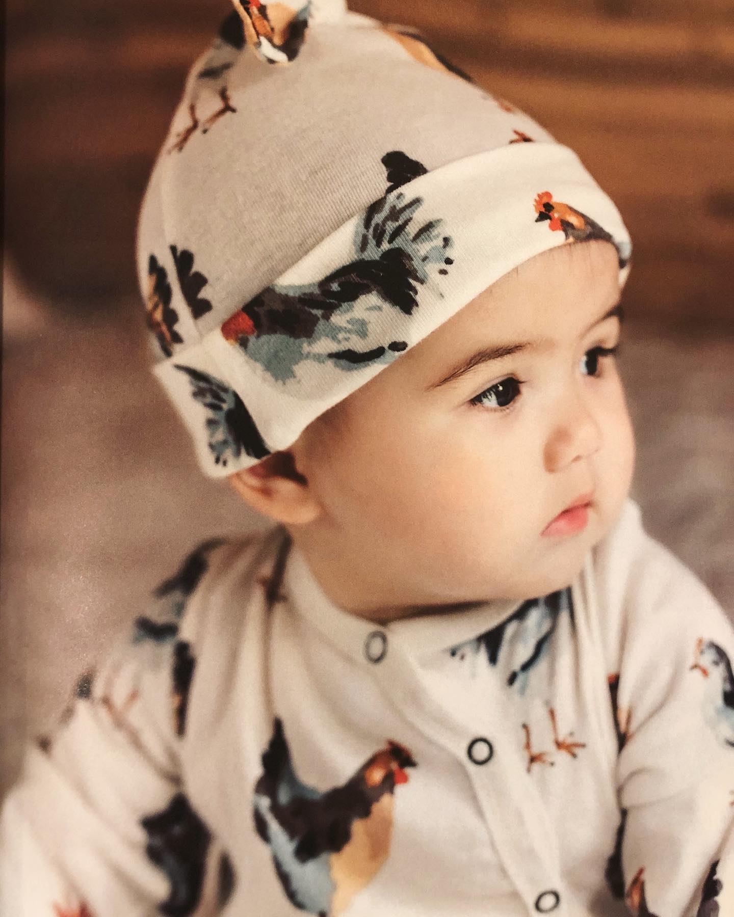 A baby wearing a hat with chickens on it