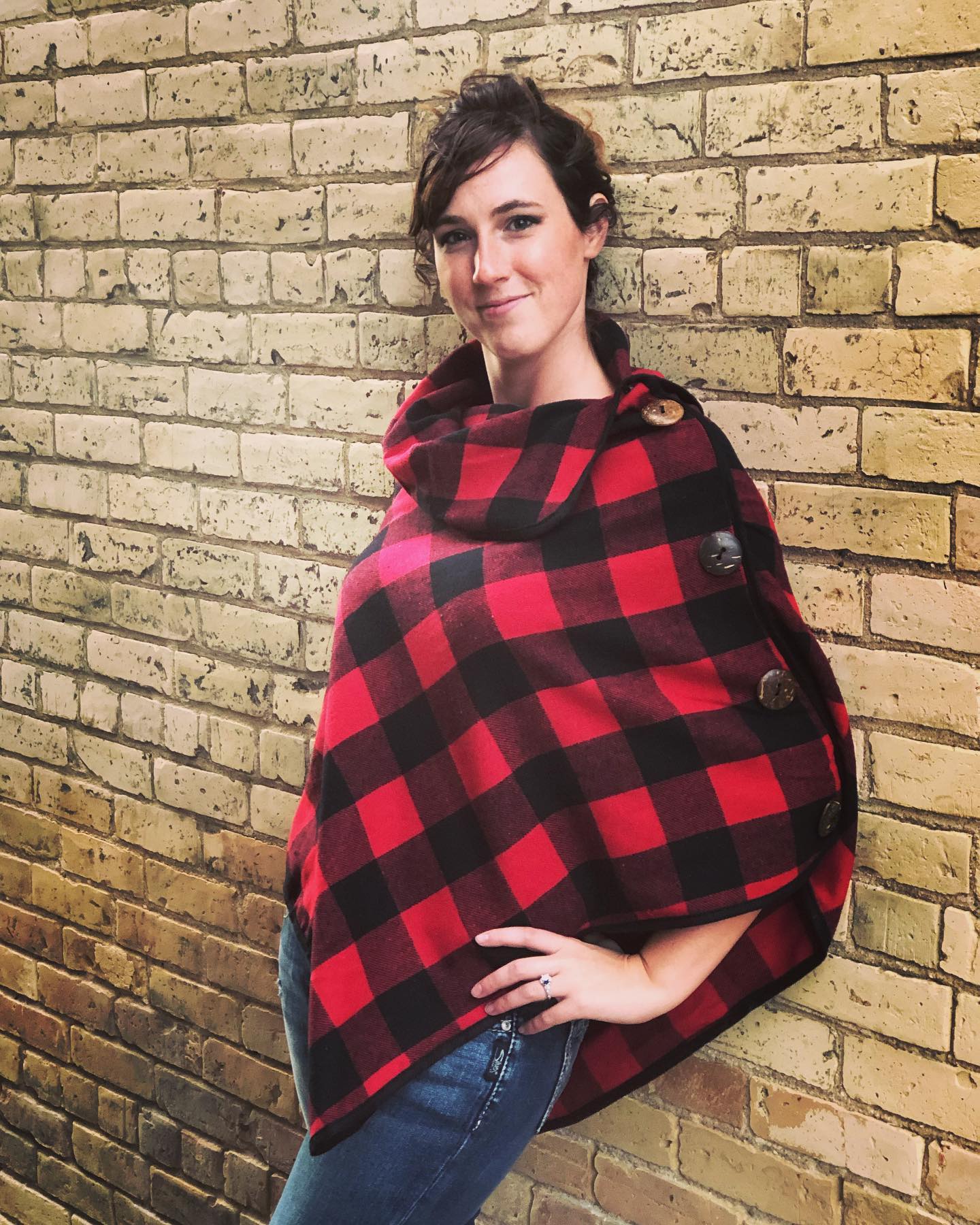 A woman wearing a plaid poncho is standing in front of a brick wall