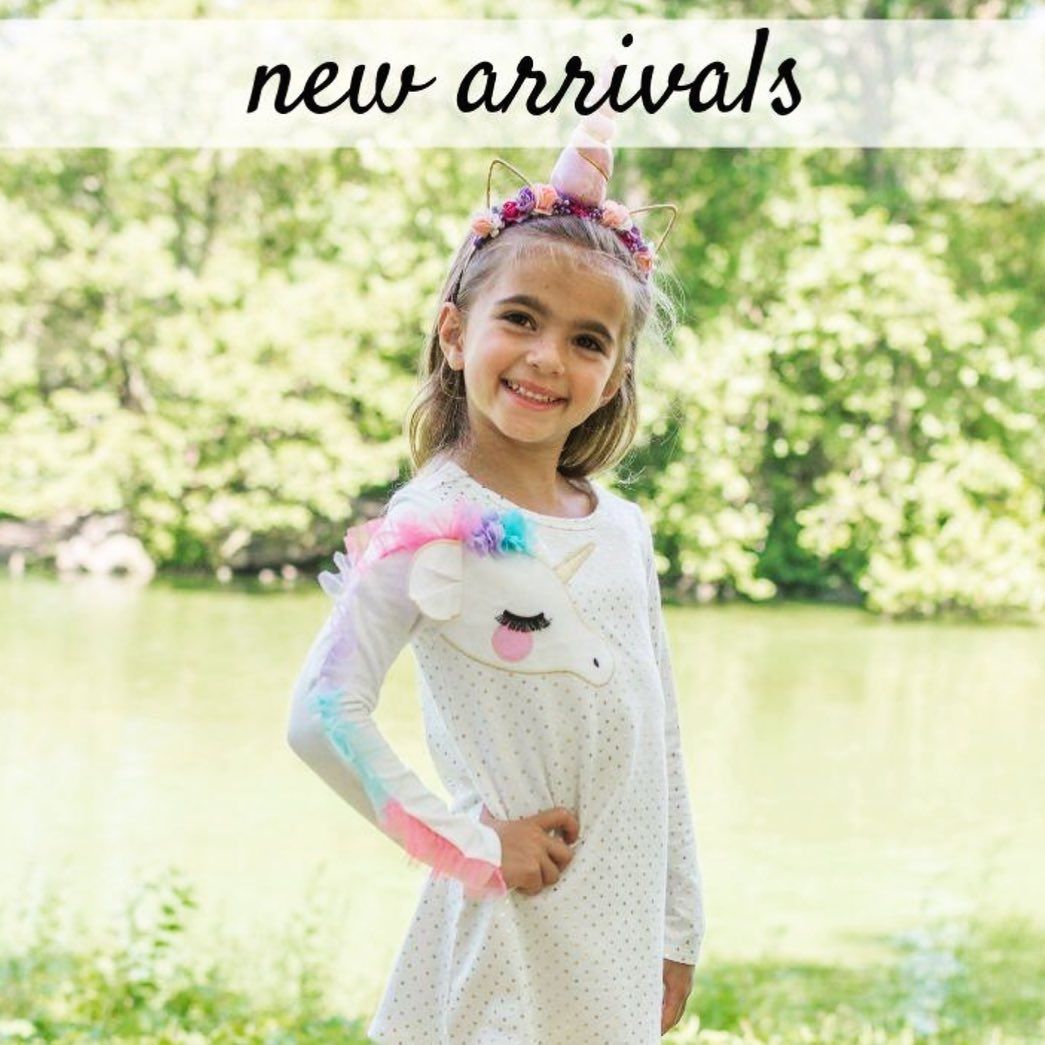 A little girl is wearing a unicorn dress and a unicorn headband.