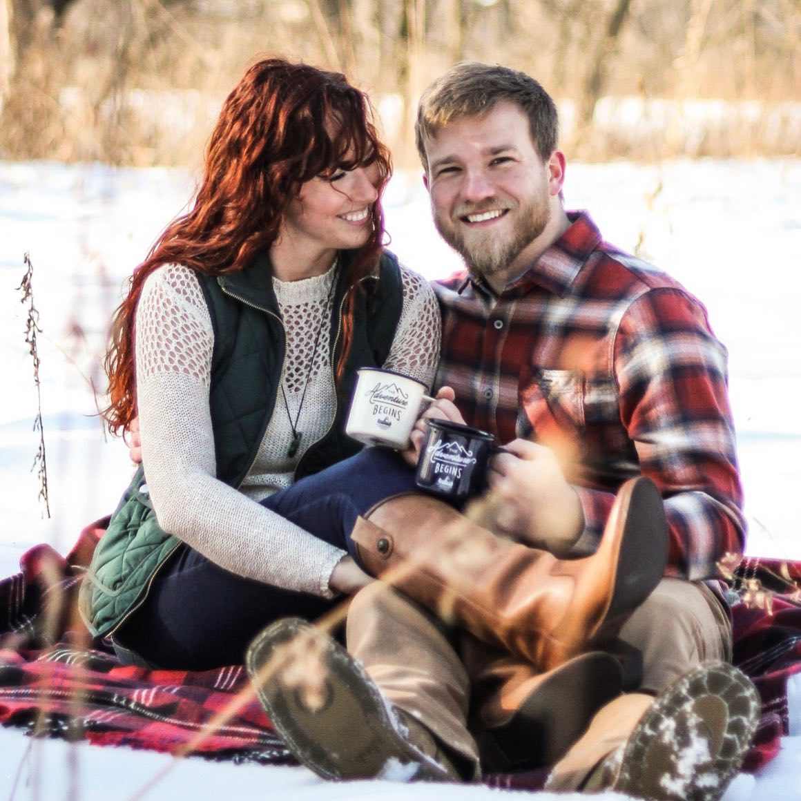A man and a woman are sitting on a blanket in the snow