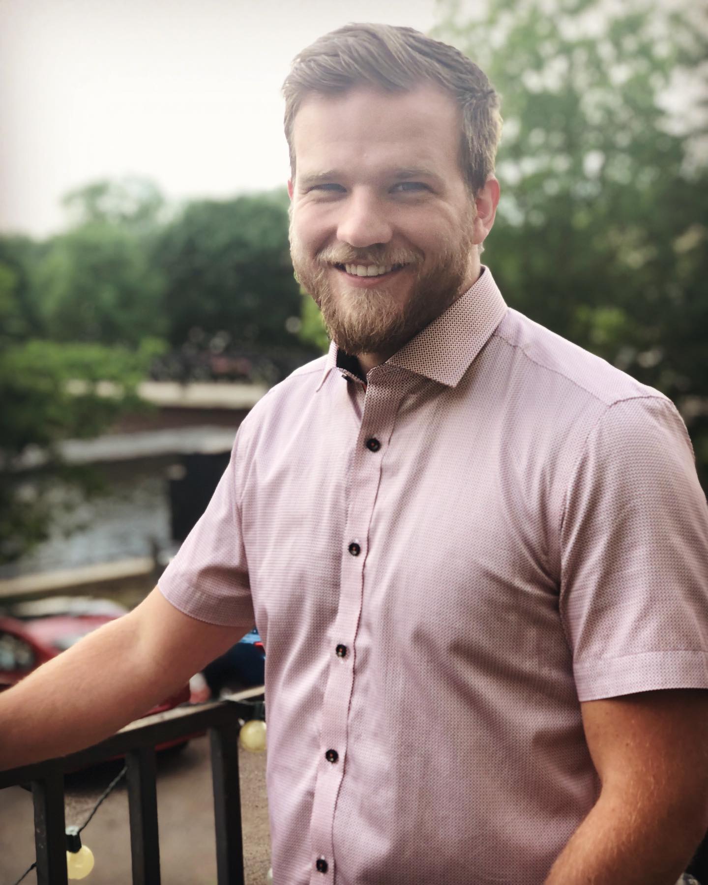 A man in a pink shirt is standing next to a railing and smiling.
