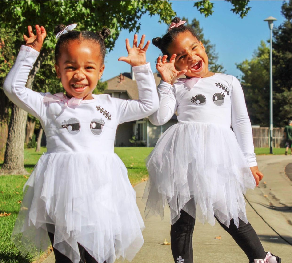 Two little girls dressed as ghosts are standing next to each other on a sidewalk